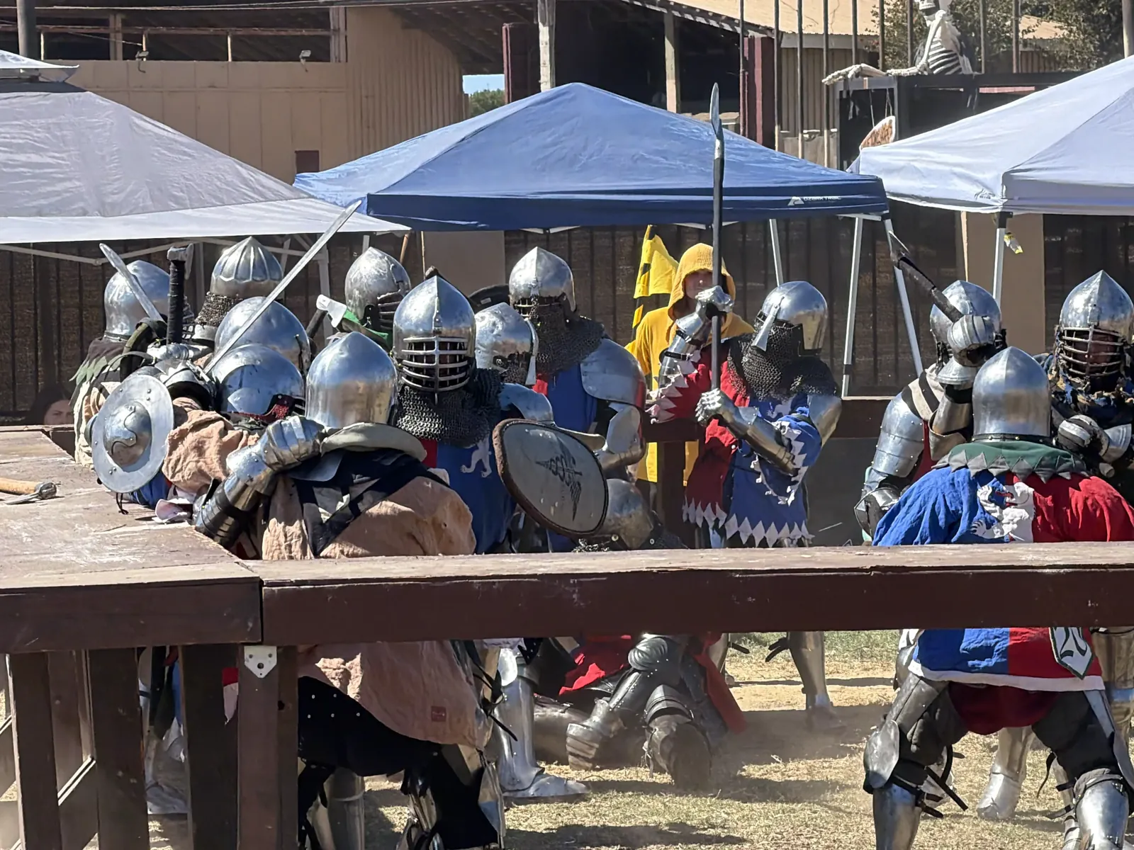 Armored fighters with swords, shields and a polearm clashing behind a wooden rail at the Oktoberfest medieval combat, Ventura County Fairgrounds